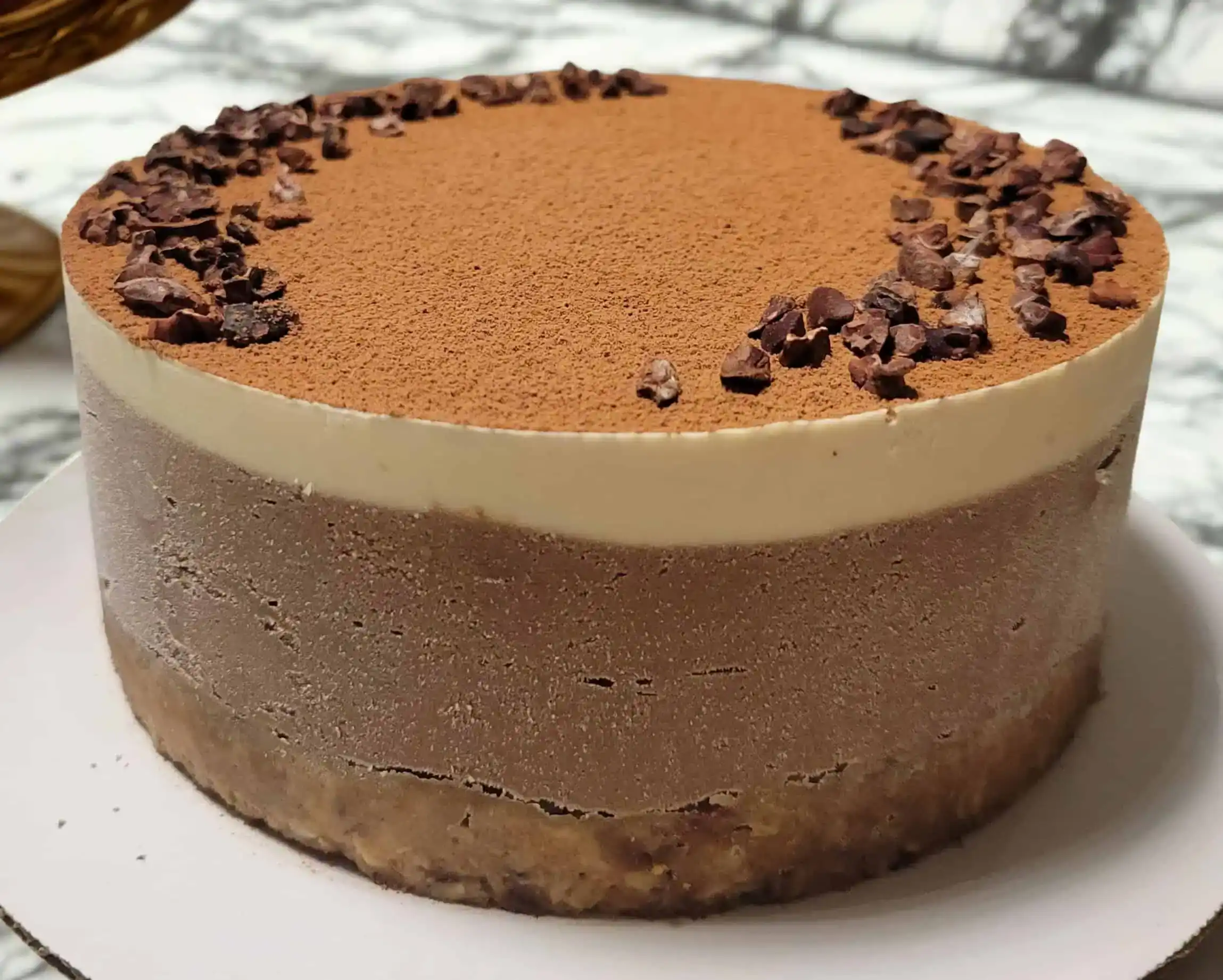 Vegan Tiramisu Cake Raw vegan espresso mocha cake with a walnut-date crust, topped with cocoa powder and cacao nibs, featuring smooth cashew cream layers in mocha and espresso flavors.