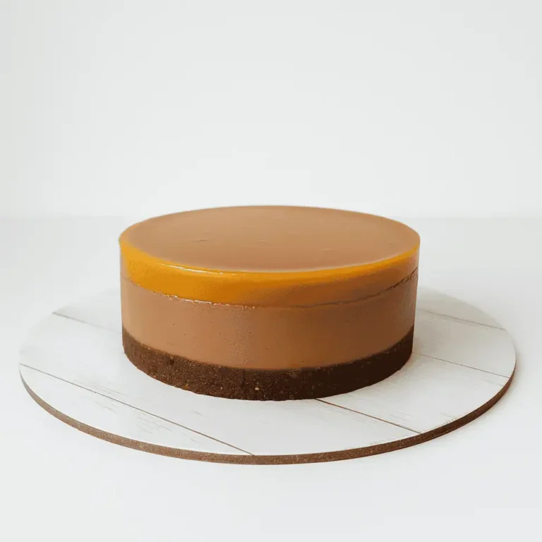 Vegan passion fruit cake with a chocolate layer and glossy passion fruit glaze, displayed on a white wooden cake board against an off-white background.